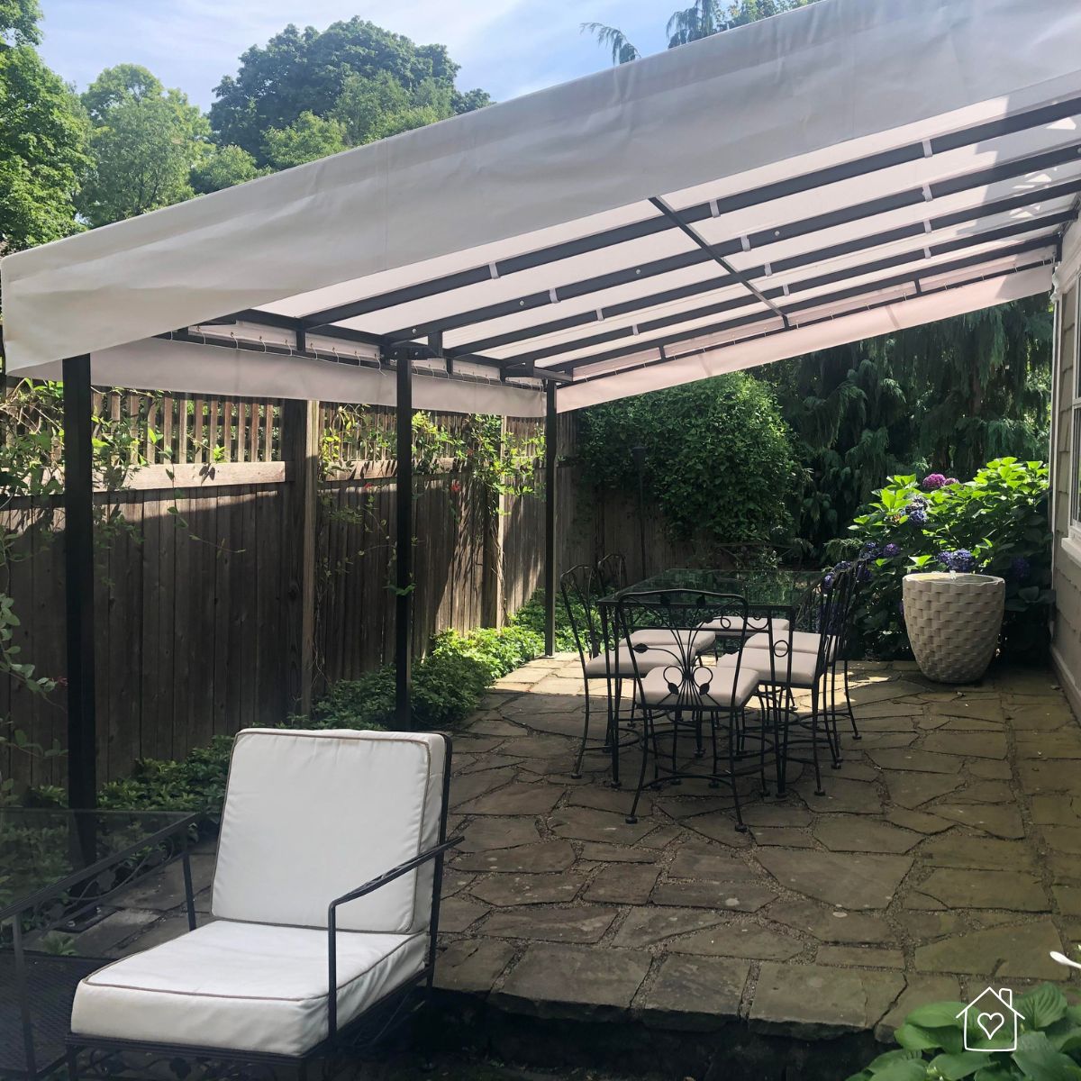 Sleek white awning installed over a backyard patio with wrought iron furniture and stone flooring.
