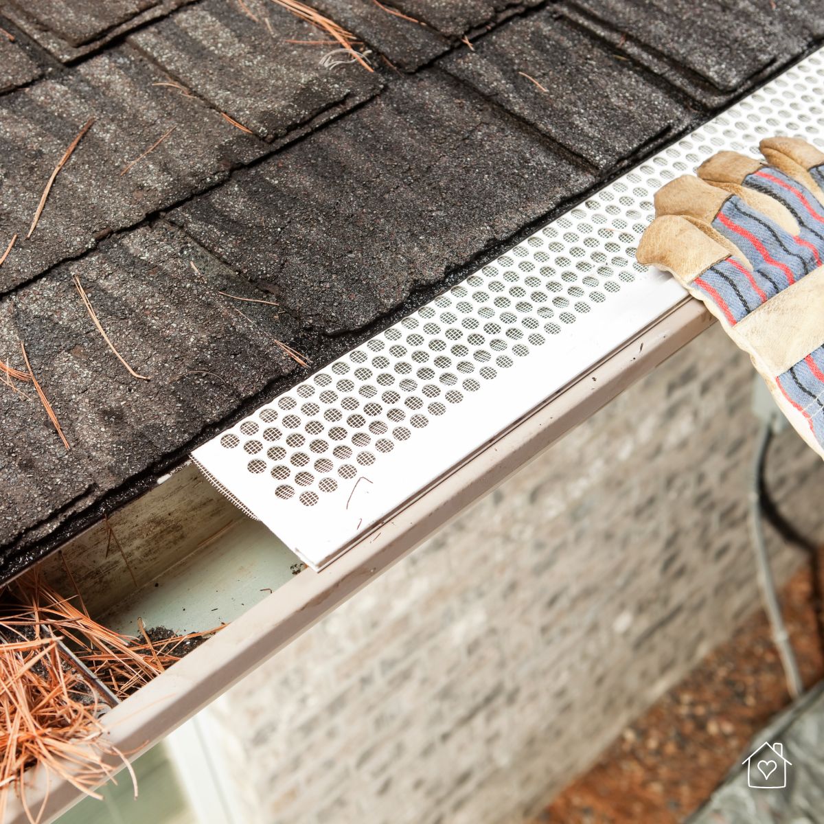 Gloved hands installing a leaf guard on roof gutters to prevent blockages and water overflow.
