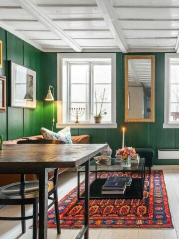 A cozy, eclectic living space with forest green walls, layered artwork, a bold rug, and a mix of textures and vintage finds for a personalized vibe.