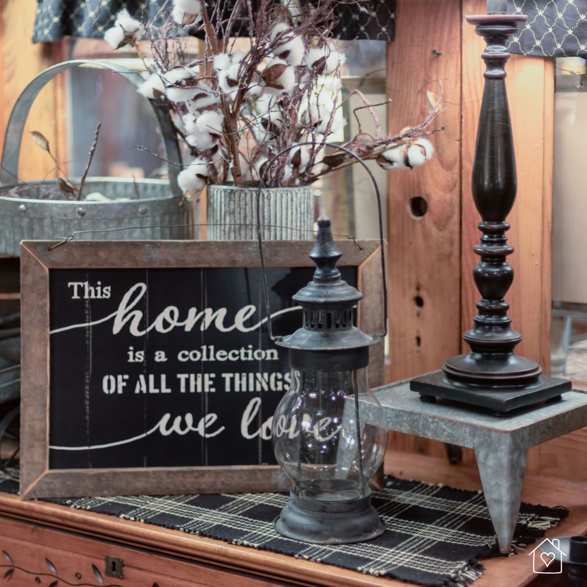 Farmhouse-style home decor arrangement featuring a vintage lantern, rustic framed sign, and cotton stem centerpiece.