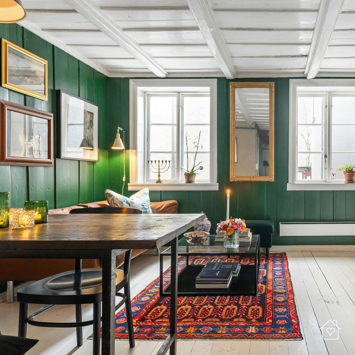 A cozy, eclectic living space with forest green walls, layered artwork, a bold rug, and a mix of textures and vintage finds for a personalized vibe.