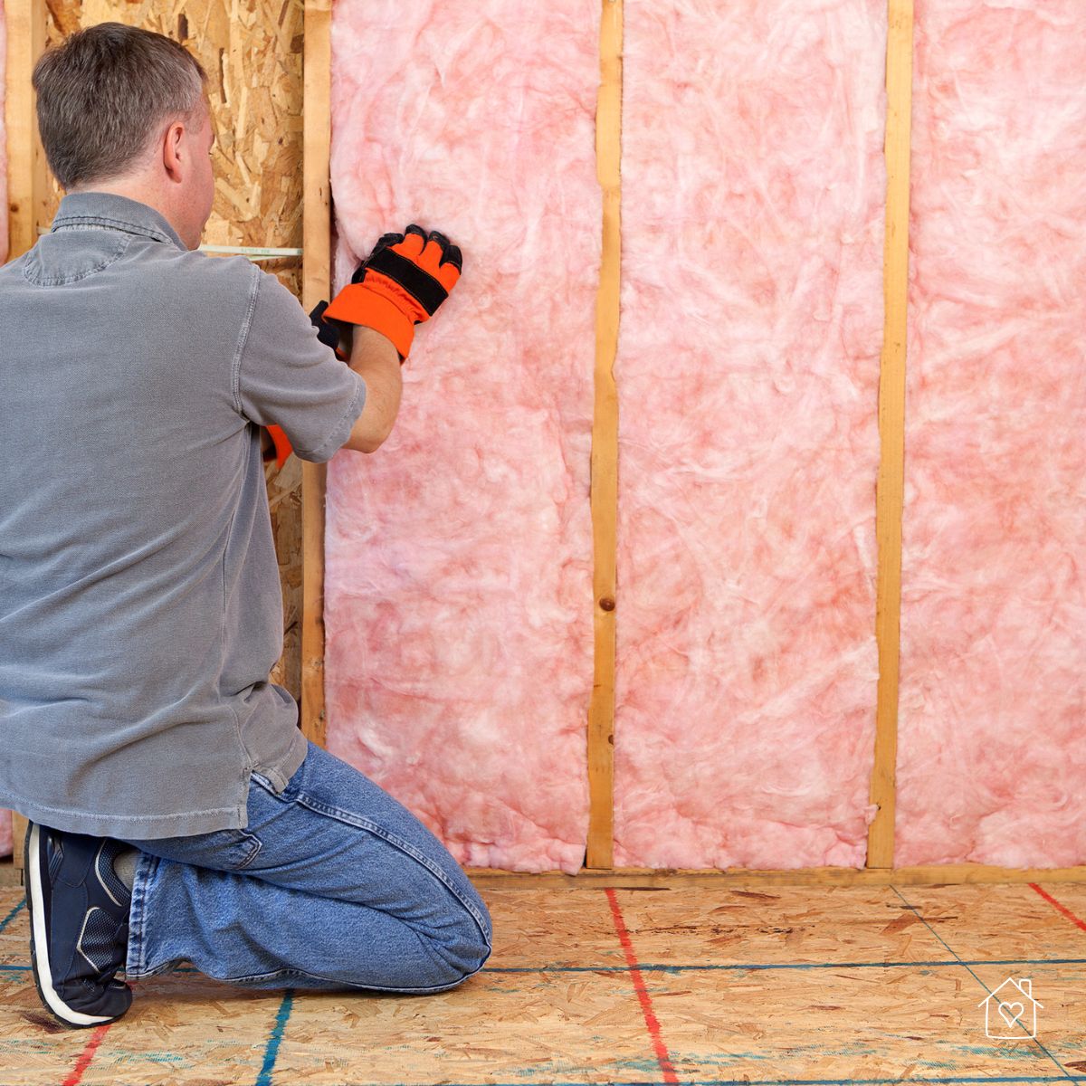 Worker installing pink fiberglass insulation in home walls to improve energy efficiency and prevent weather damage.