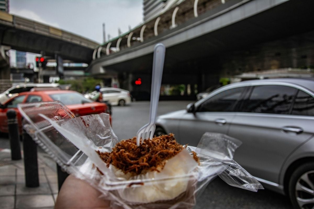 A hand holding a container of traditional Emirati street food with shredded meat over rice, taken on a bustling city street in the UAE.