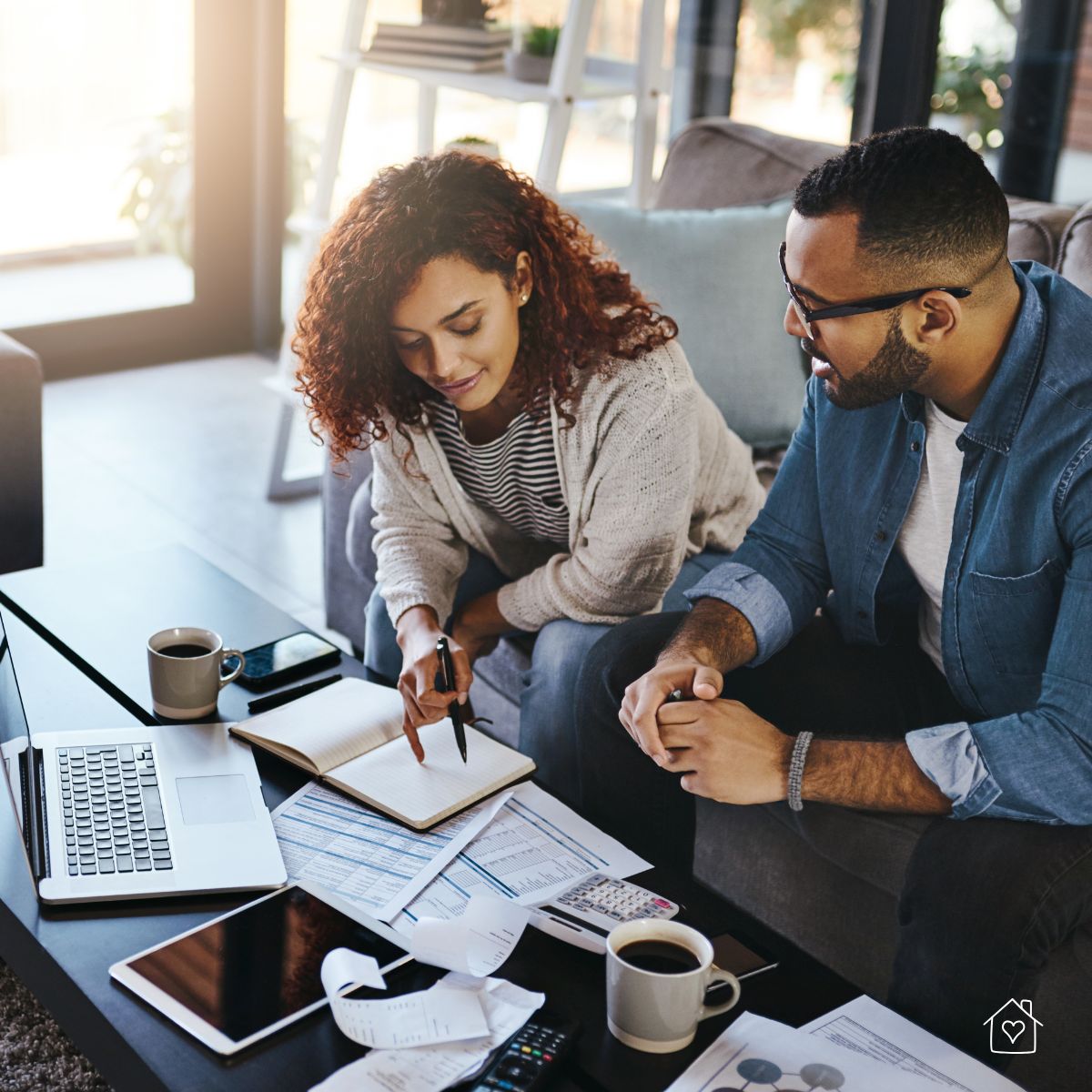 A young couple sitting together at a coffee table with a laptop, receipts, and paperwork while discussing personal loan options.