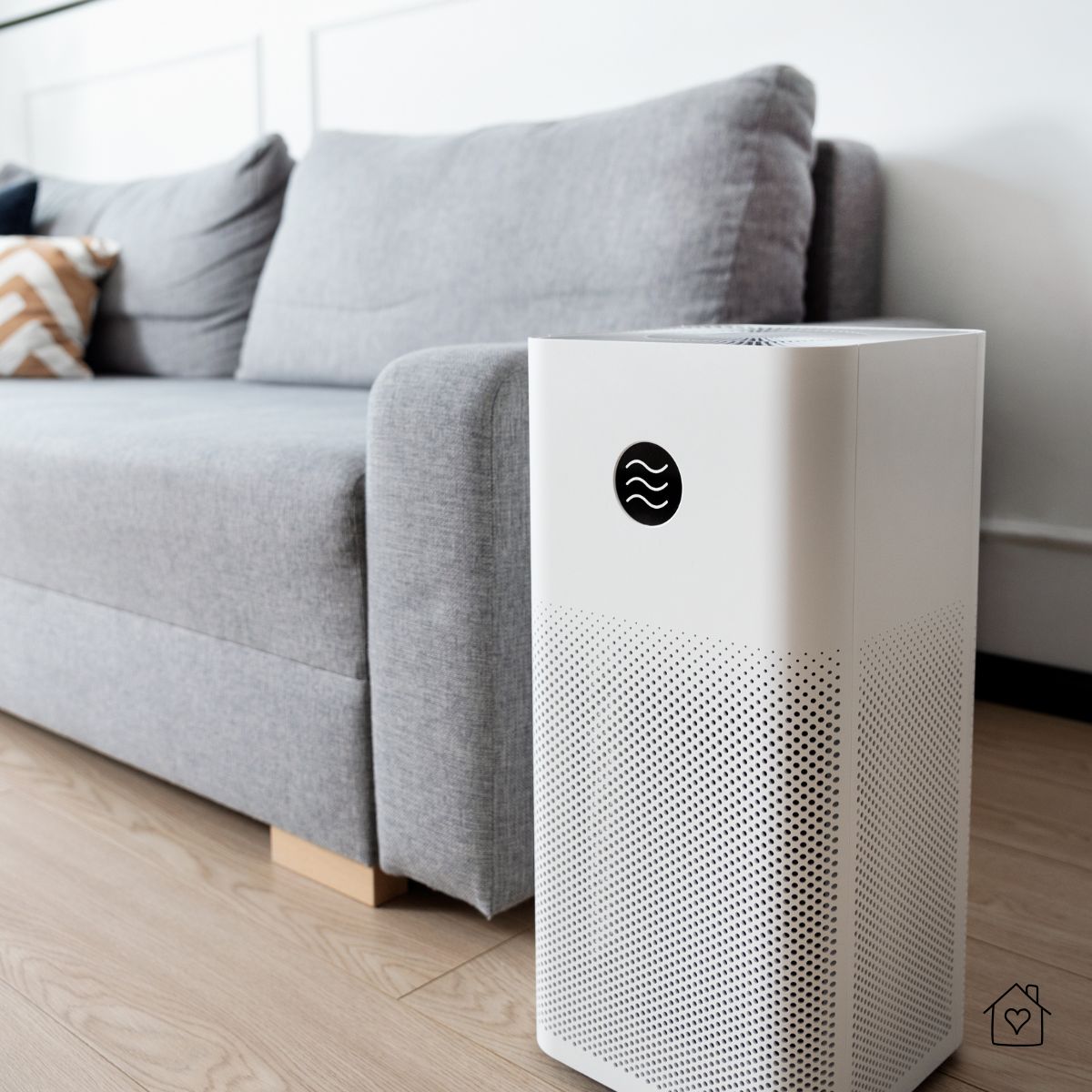 Modern air purifier placed in front of a gray couch in a clean living room.