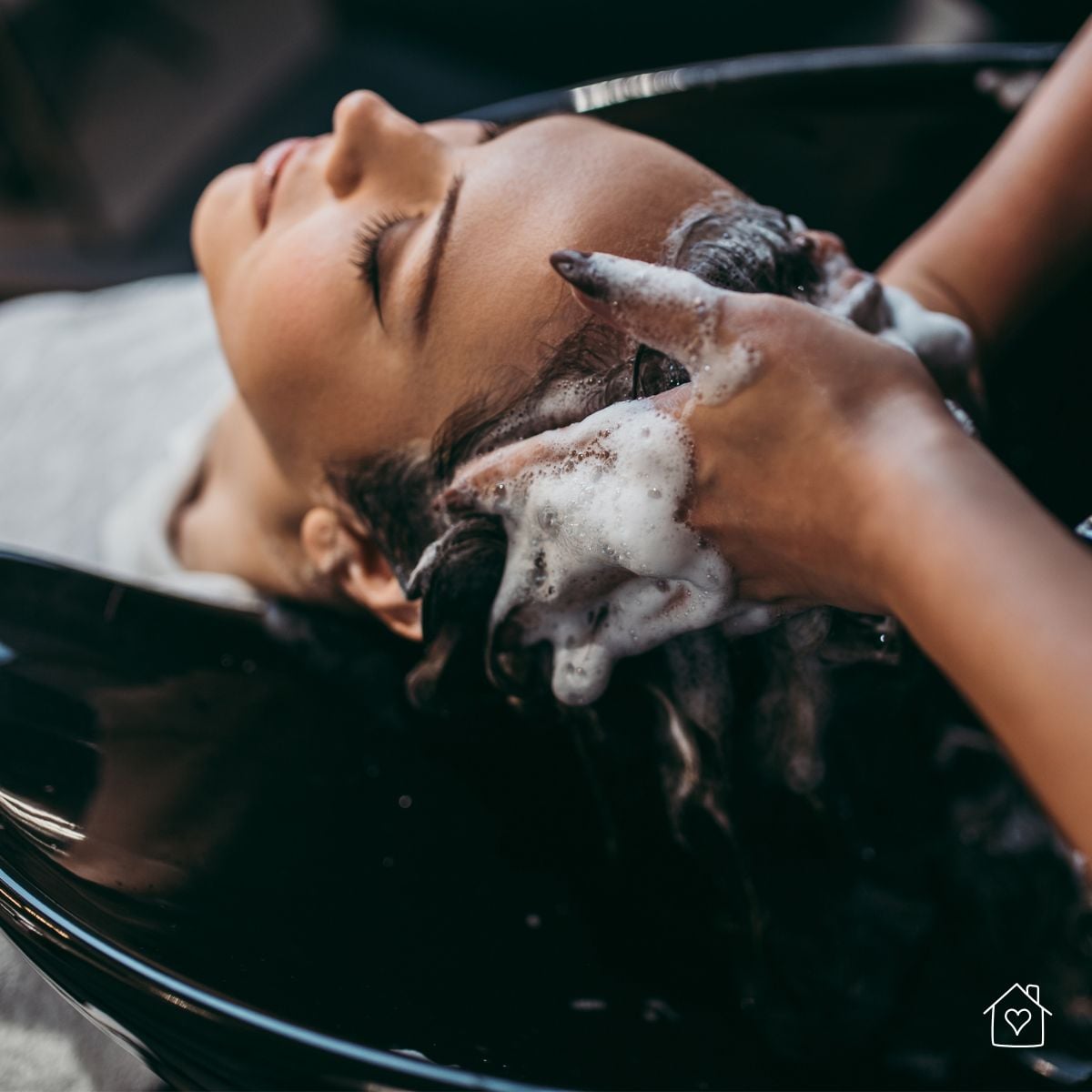 Close-up of a woman enjoying a professional hair wash with gentle scalp massage in a sleek black basin.
