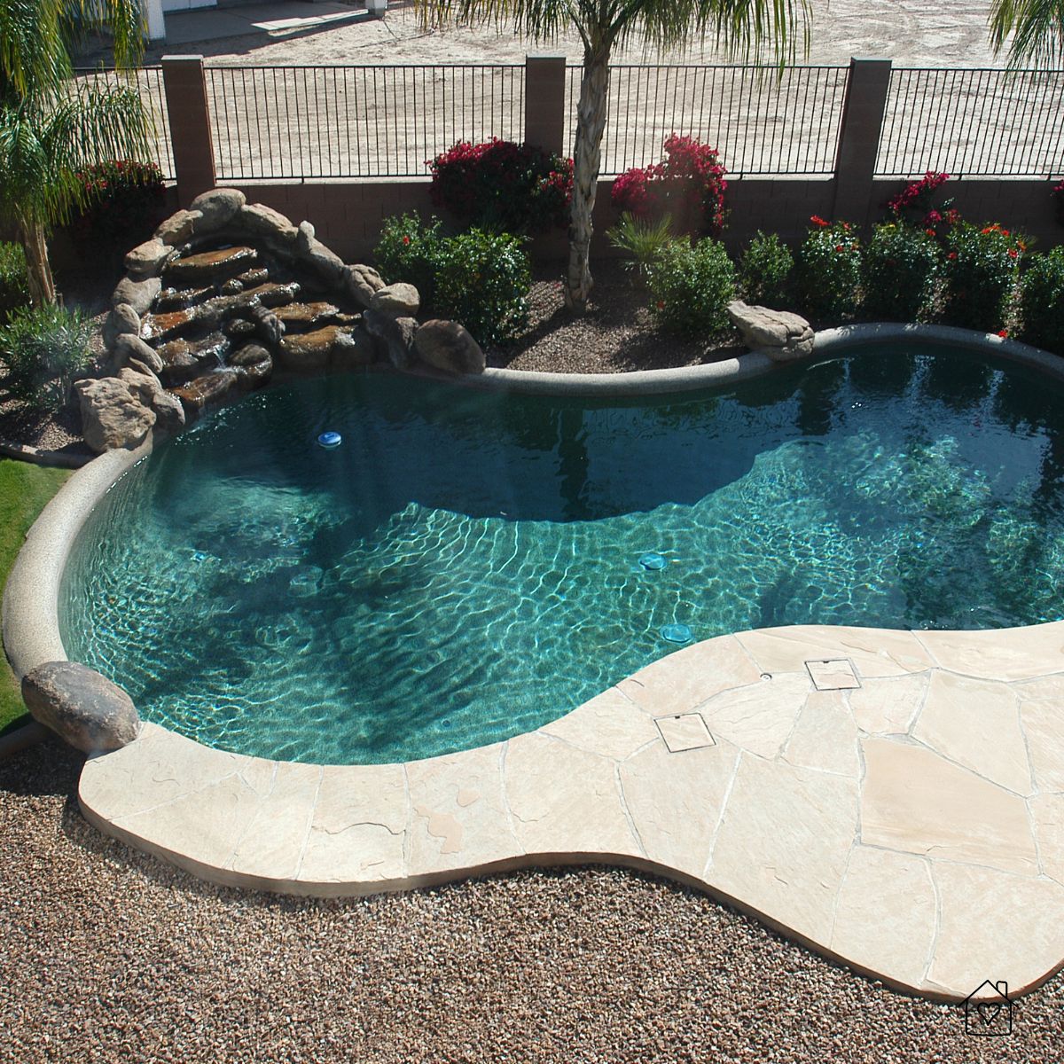 Beautiful curved swimming pool with rock waterfall feature and stone decking, an inviting area ideal for upgrading with rubber surfacing