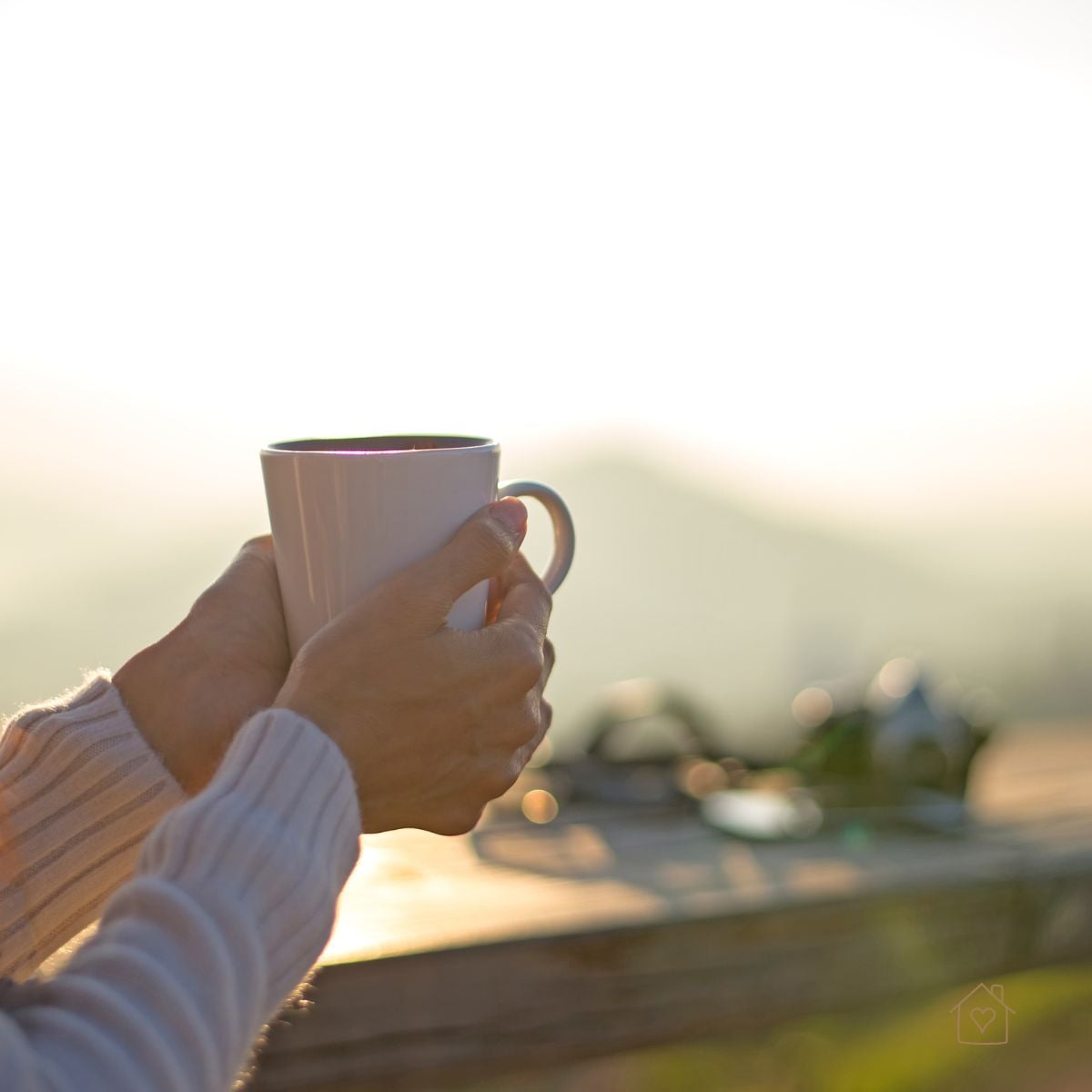 Hands holding a coffee mug outdoors with sunrise in the background, symbolizing a mindful start to the day.