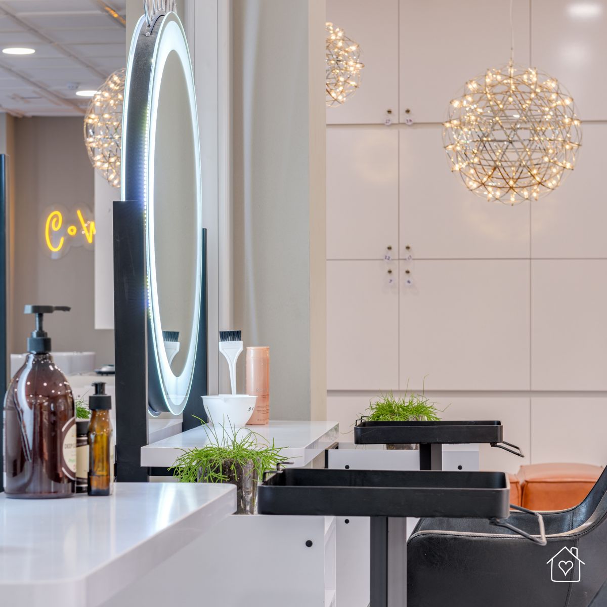 Modern hairdressing station in a home salon with illuminated round mirror, hair care products, and decorative lighting.
