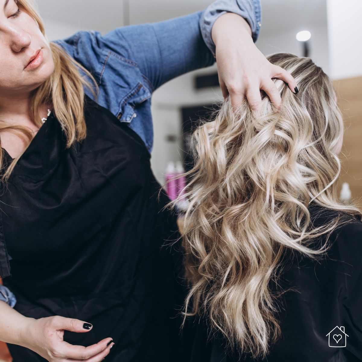 Hair stylist styling long blonde hair into voluminous waves inside a home-based beauty salon.