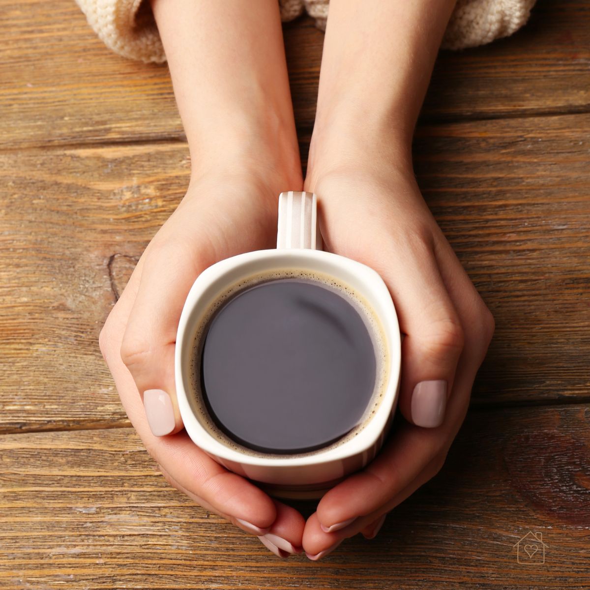 Close-up of hands holding a steaming cup of black coffee on a rustic wooden table.