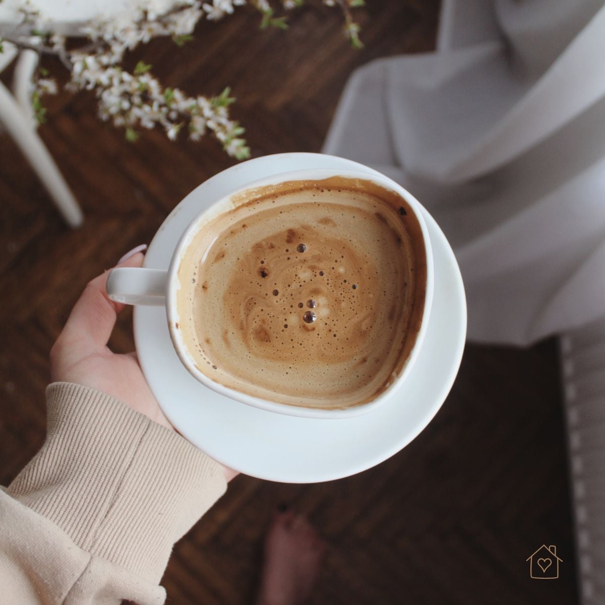 Overhead view of a hand holding a cup of frothy coffee in a cozy home setting.