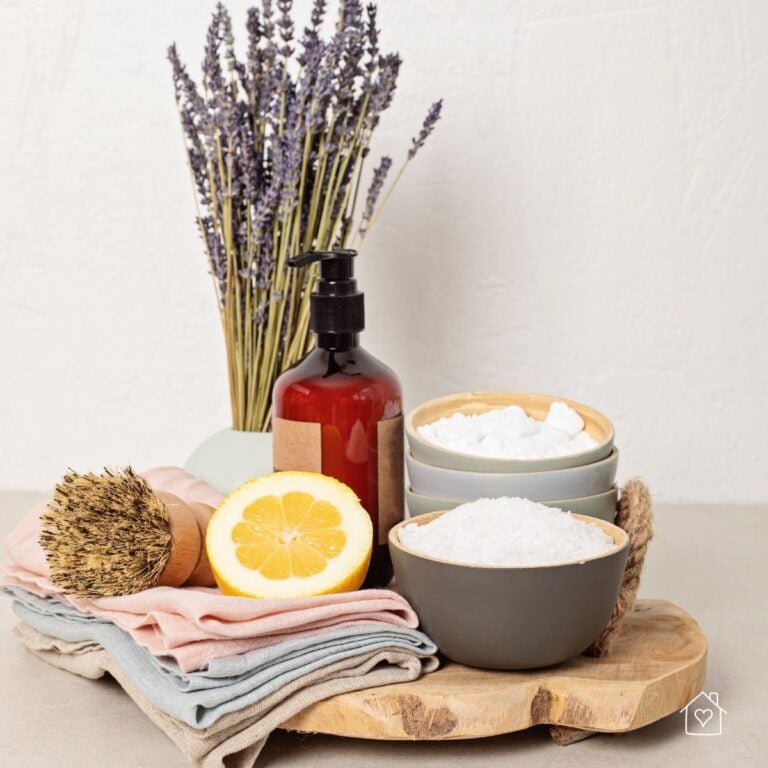 A natural cleaning kit including lemon, baking soda, salt, a brush, and cloths arranged with lavender on a wooden board.