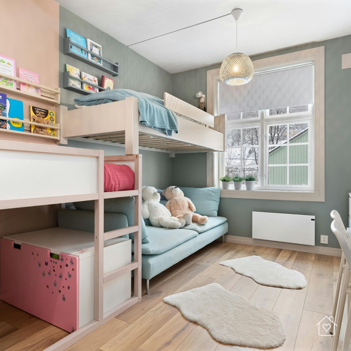 Light wood bunk bed with pastel blue bedding, sofa underneath, and wall-mounted bookshelves in a modern children’s bedroom.