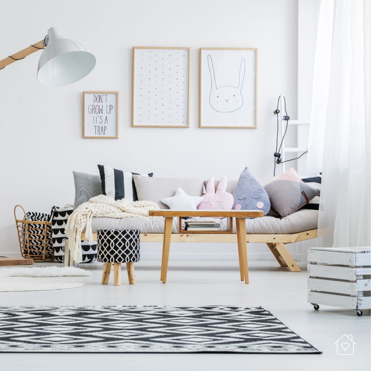 Light wood sofa with pastel cushions, framed wall art, and black-and-white patterned rug in a bright children’s play space.