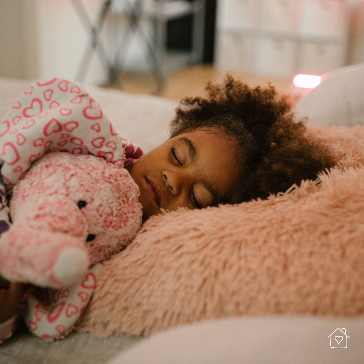 Young girl peacefully sleeping on a fluffy peach pillow while holding a pink stuffed elephant in a cozy bedroom setting.