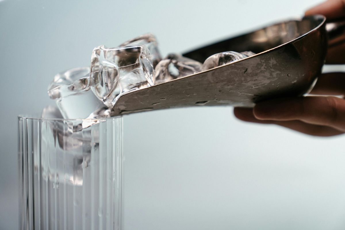 A scoop pouring ice cubes into a clear glass, illustrating the freezing method for gum and wax stain removal from carpet.