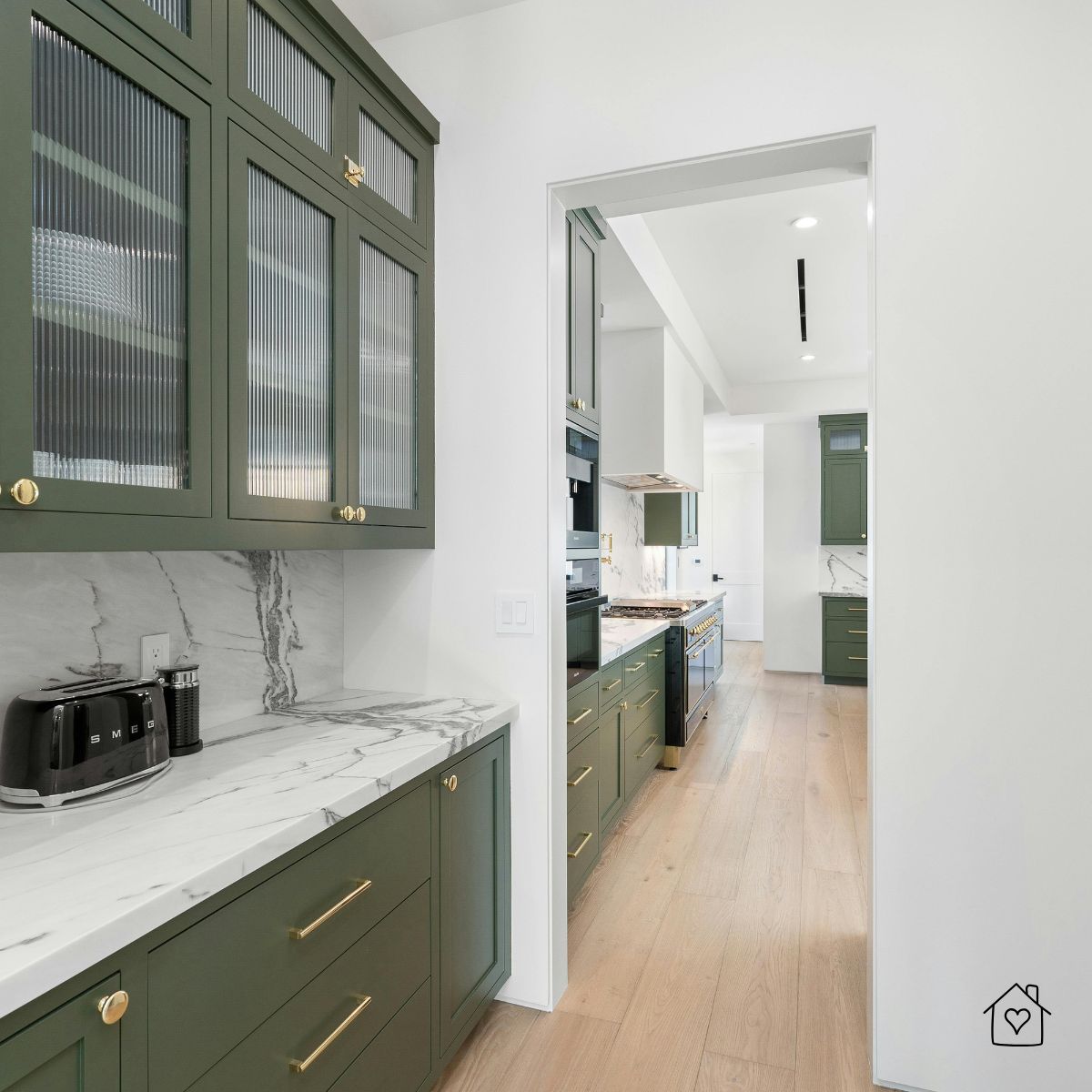 Stylish green kitchen cabinets with gold knobs and pulls paired with marble counters.