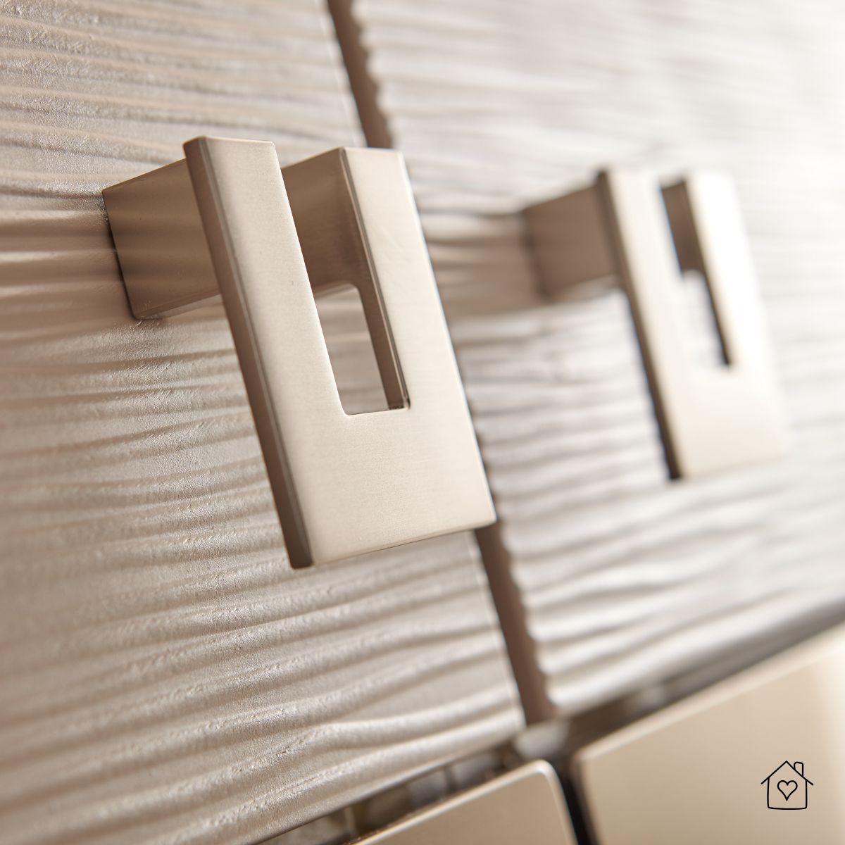 Close-up of modern brushed nickel cabinet pulls on textured wood surface.