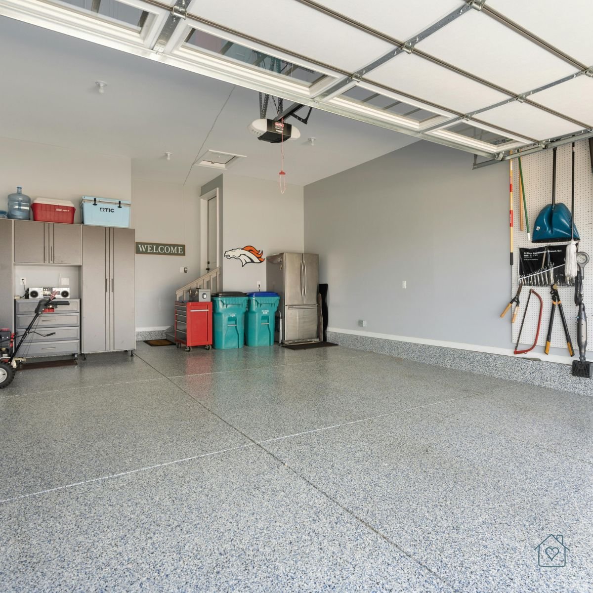 Clean and organized garage with cabinets, storage bins, and a polished epoxy floor ready for conversion into a home office or gym.