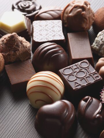 Close-up of assorted luxury chocolates—dark, milk, and white truffles and pralines—arranged on dark wood for a curated chocolate collection.