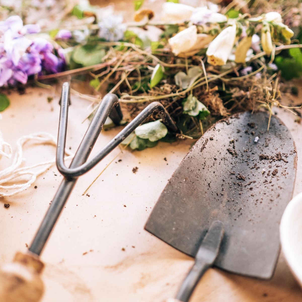 Close-up of metal hand tools with dirt, surrounded by dried flowers and garden clippings.