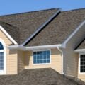 Two-story home with architectural asphalt shingles and white gutters under a clear blue sky.
