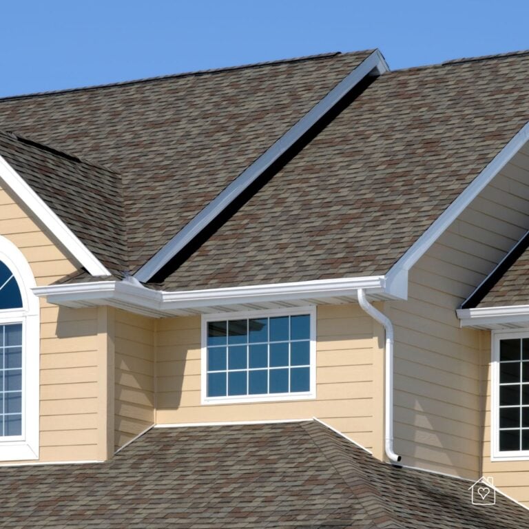 Two-story home with architectural asphalt shingles and white gutters under a clear blue sky.