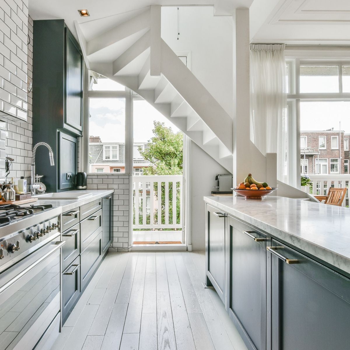 Modern kitchen with white flooring, large windows, and sheer curtains allowing natural light to brighten the space.