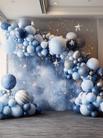 A balloon garland in shades of blue with star decorations and string lights, styled against a cosmic night sky backdrop for a magical starry night party.