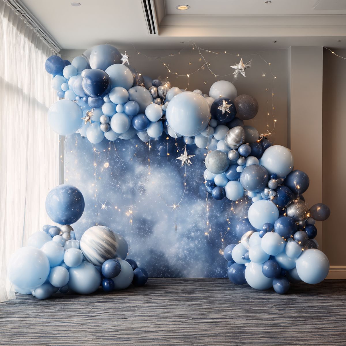 A balloon garland in shades of blue with star decorations and string lights, styled against a cosmic night sky backdrop for a magical starry night party.