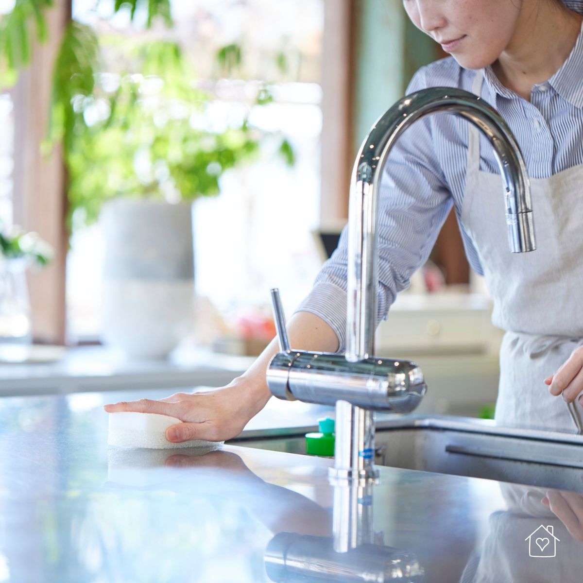Person wiping a shiny kitchen countertop near a sink with a sponge for a spotless finish.
