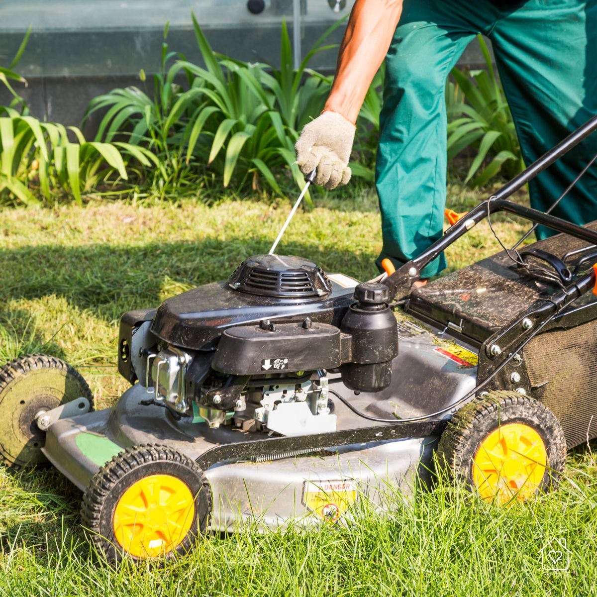 Gloved hand pulling the starter cord on a walk-behind mower, emphasizing routine blade maintenance and safety before mowing.