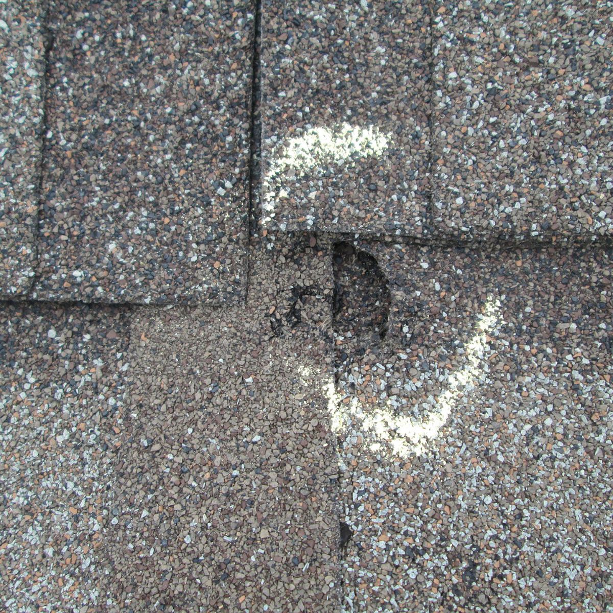 Close-up of asphalt shingles marked with chalk highlighting storm damage and missing granules after hail impact.