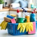 Basket filled with cleaning products, brushes, sponges, and yellow gloves on a kitchen counter.