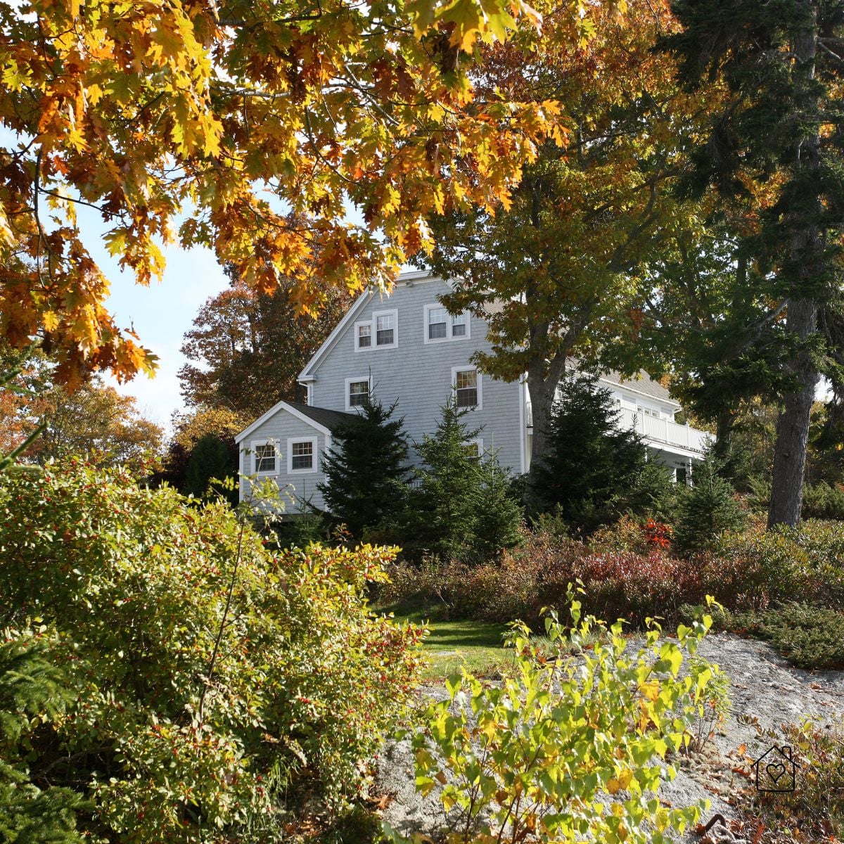 House framed by trees and shrubs showing autumn color&mdash;ideal time for pruning, weeding, and landscape TLC.