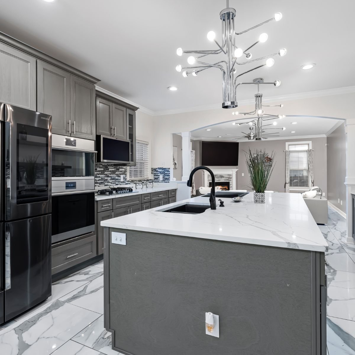 Spacious gray and white kitchen featuring glossy marble countertops, chrome fixtures, and bright pendant lighting.