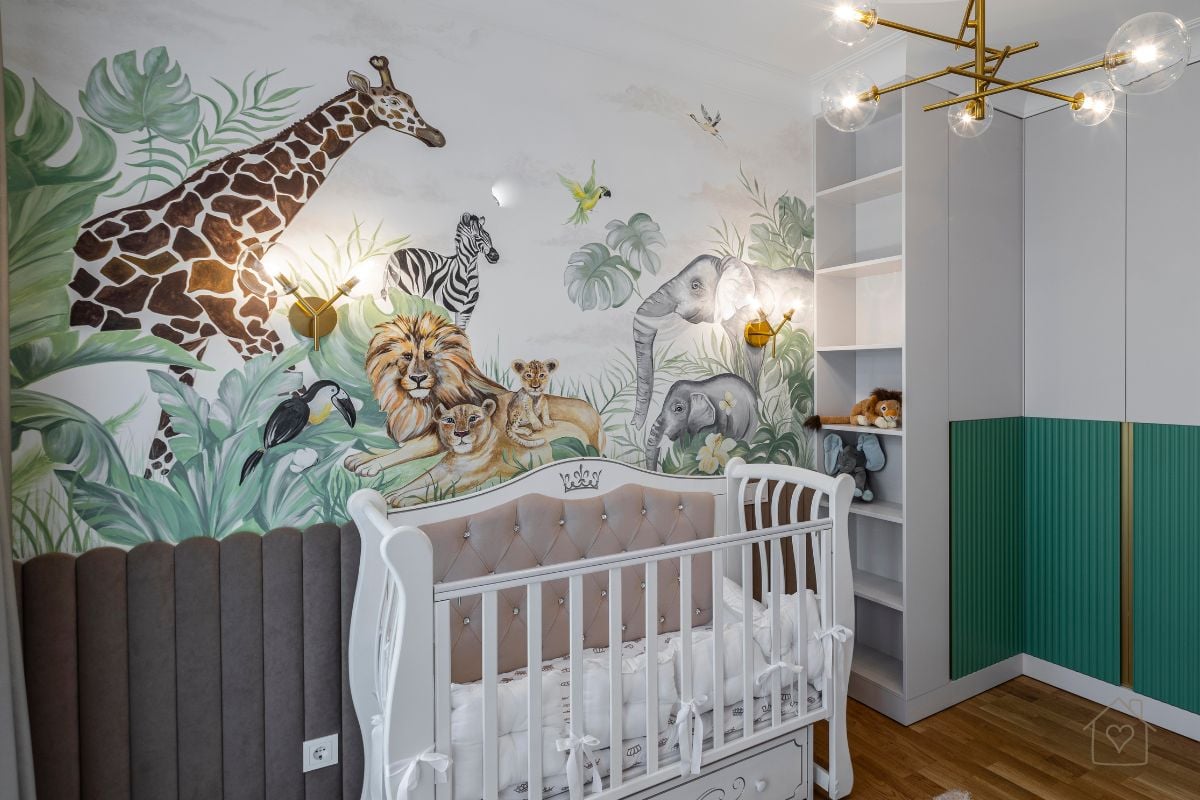 Baby nursery featuring a colorful mural of giraffe, lion, zebra, elephant, and tropical leaves behind a white crib with tufted detailing.