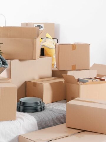 Multiple cardboard boxes filled with dishes, rugs, and personal belongings, stacked in preparation for a home move.