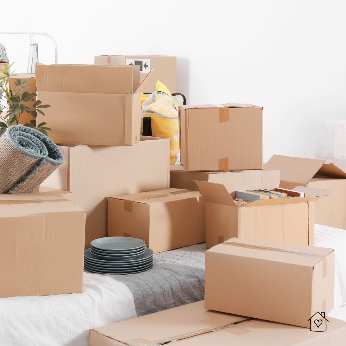 Multiple cardboard boxes filled with dishes, rugs, and personal belongings, stacked in preparation for a home move.