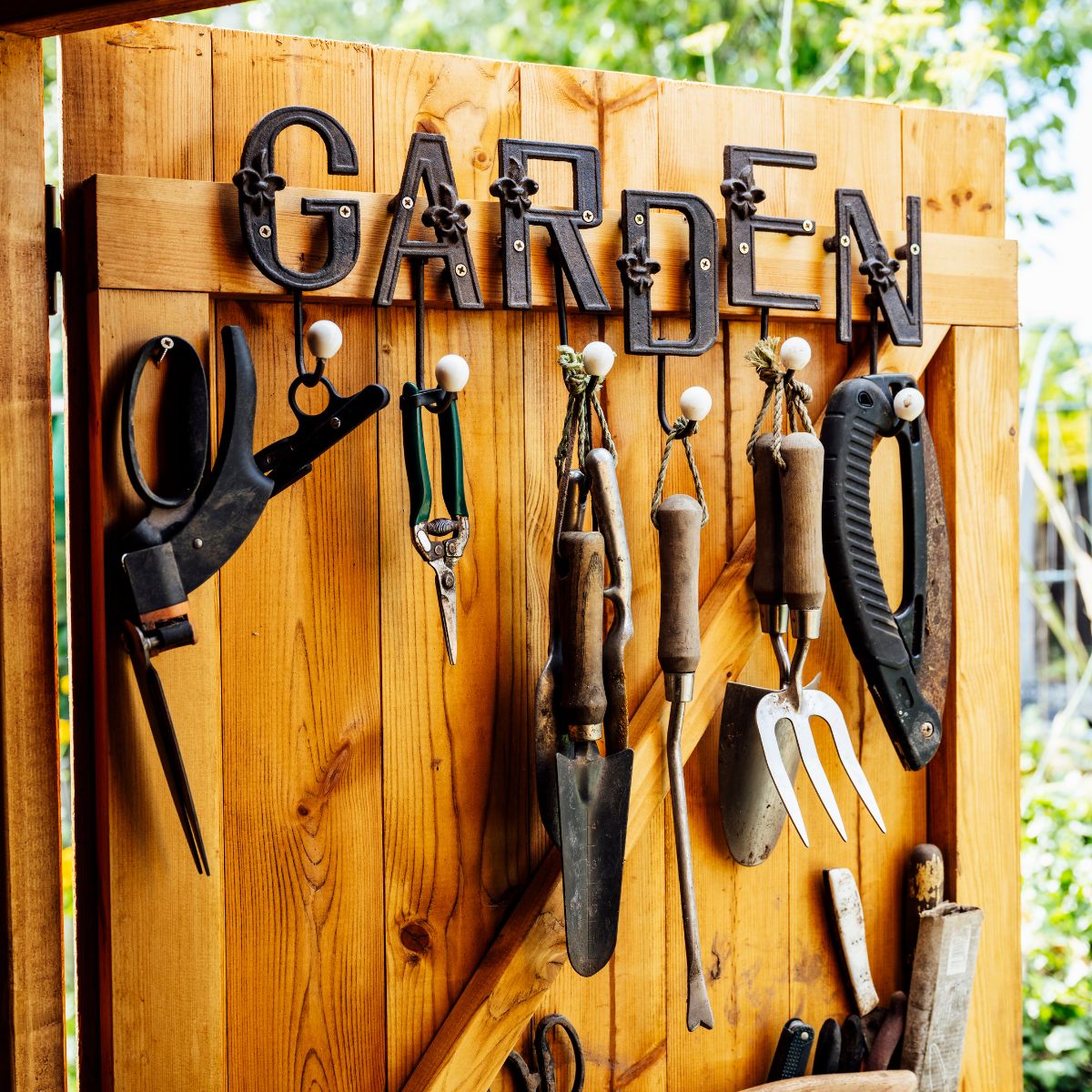 Hand tools including pruners, spades, and forks neatly hung on hooks with “GARDEN” sign.