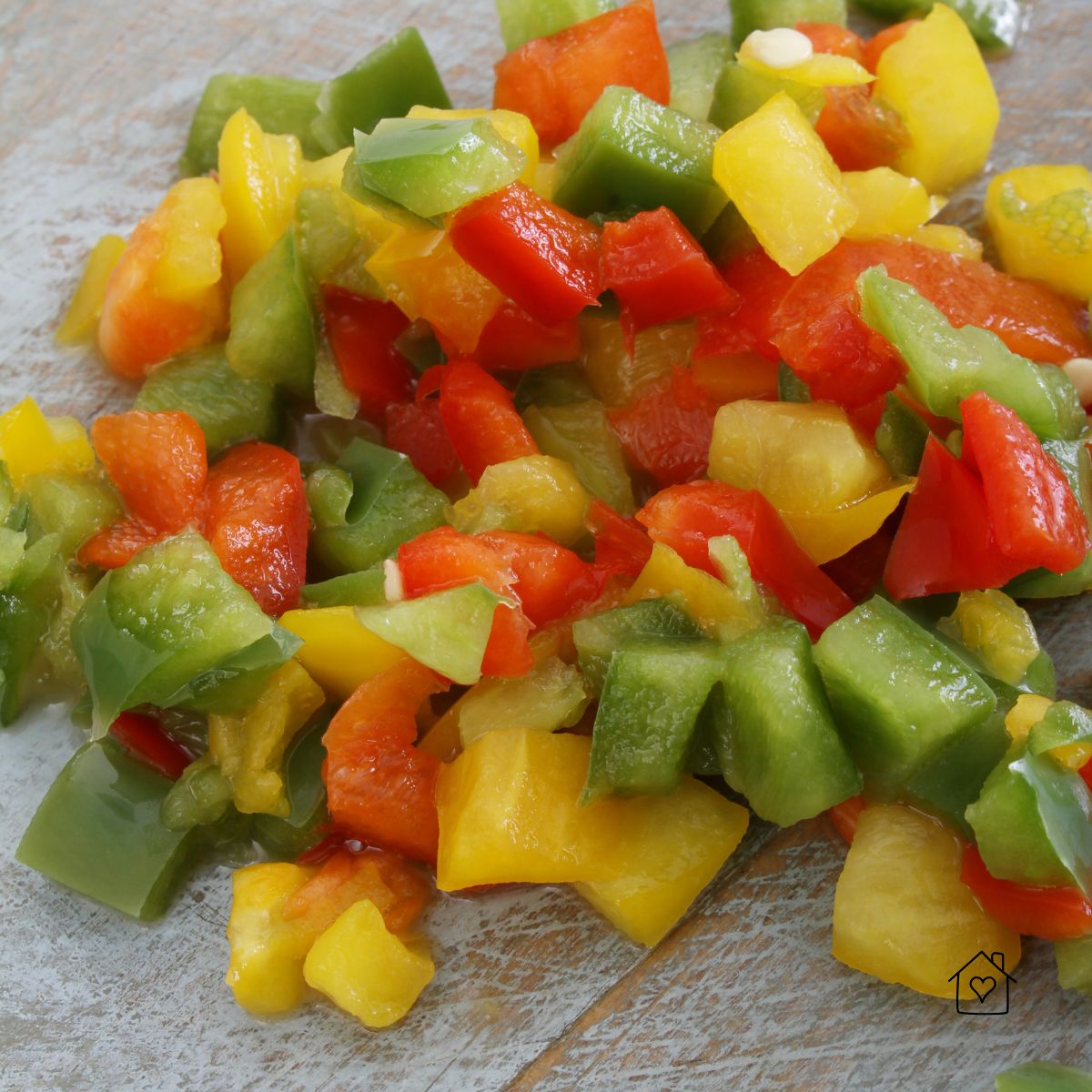 Colorful chopped bell peppers in red, yellow, and green on a rustic wooden surface.