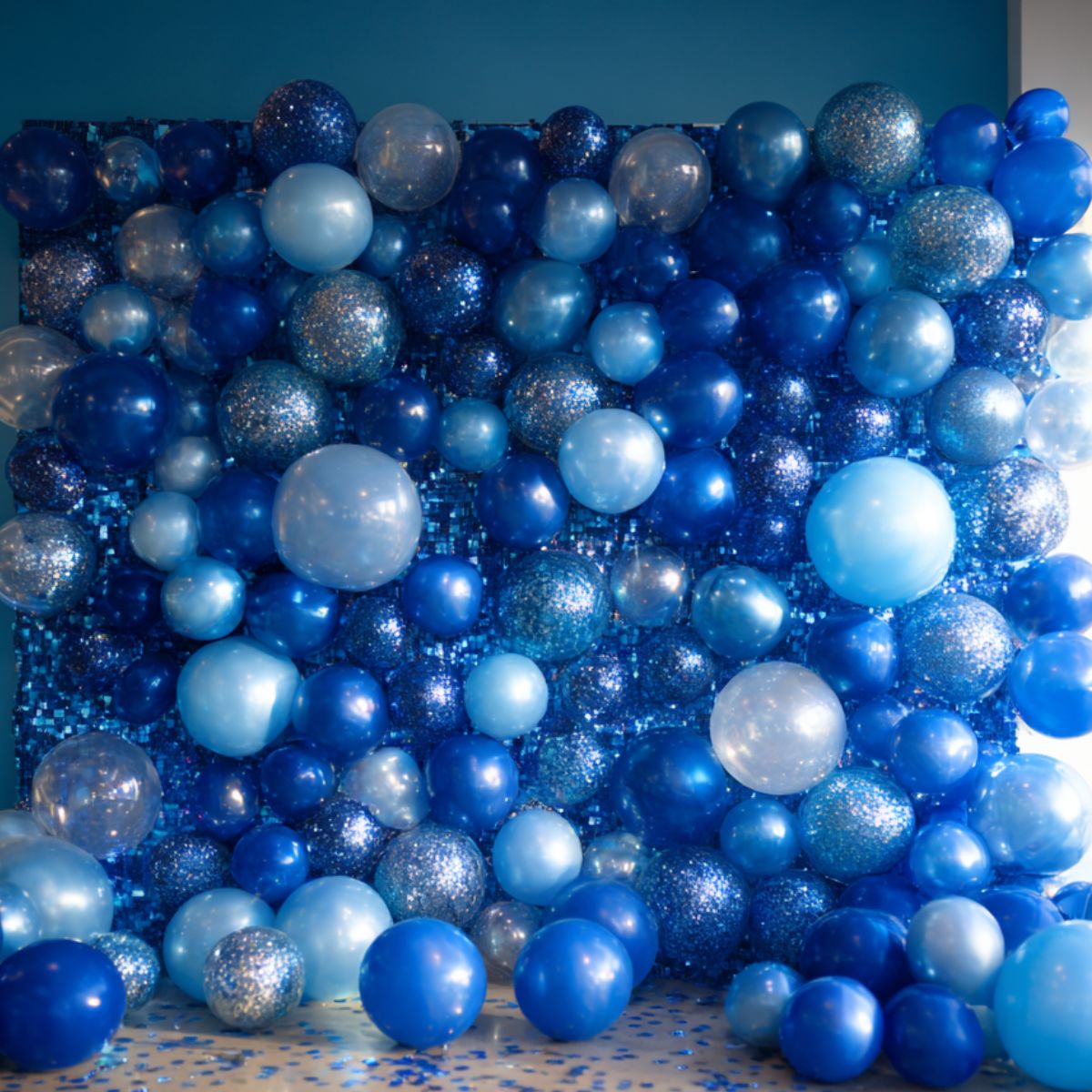 A sparkling blue balloon wall backdrop with balloons in various shades of blue, accented with glitter and confetti, perfect for photo booths or party décor.