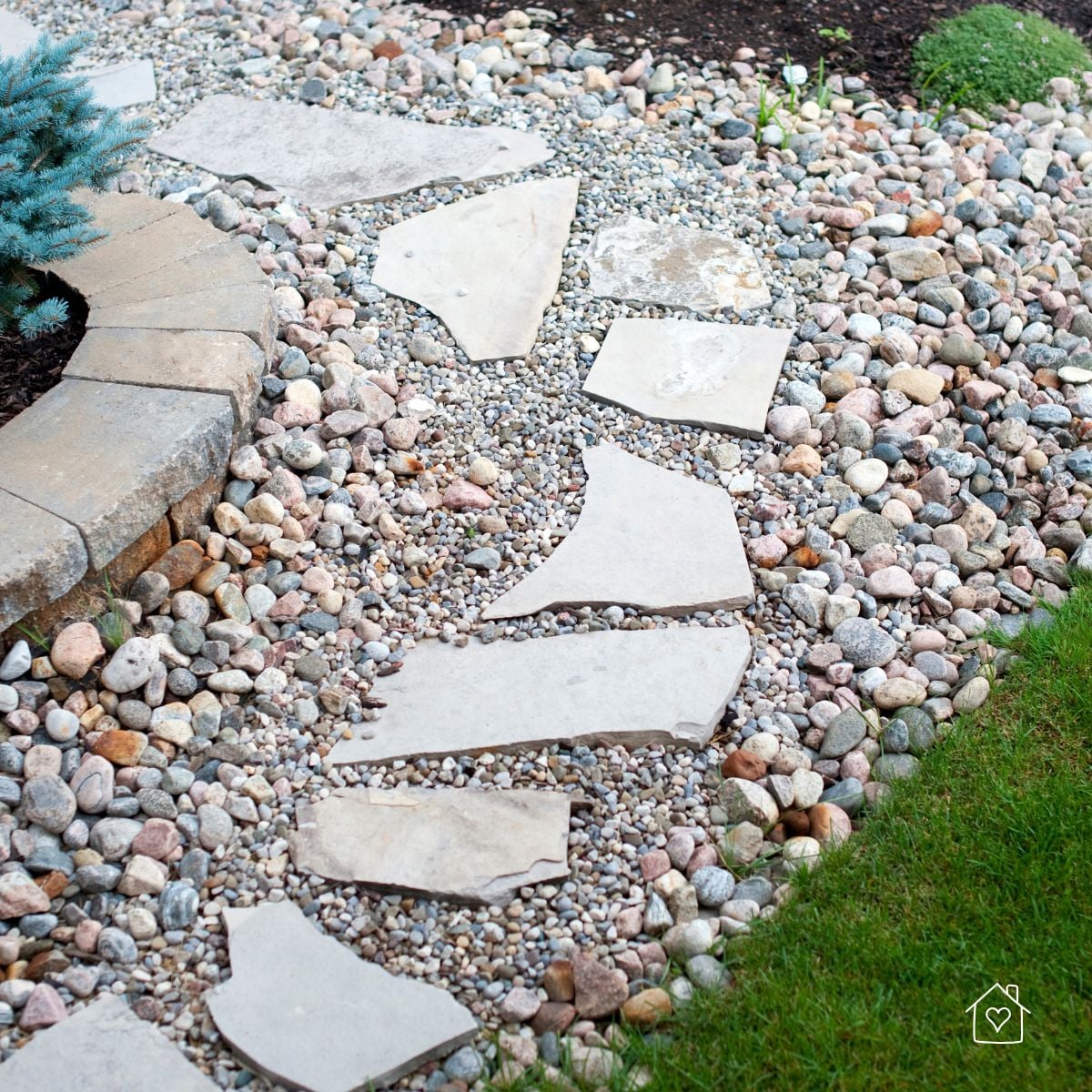 Irregular flagstone stepping stones set in pea gravel with river-rock edging curving beside a lawn.