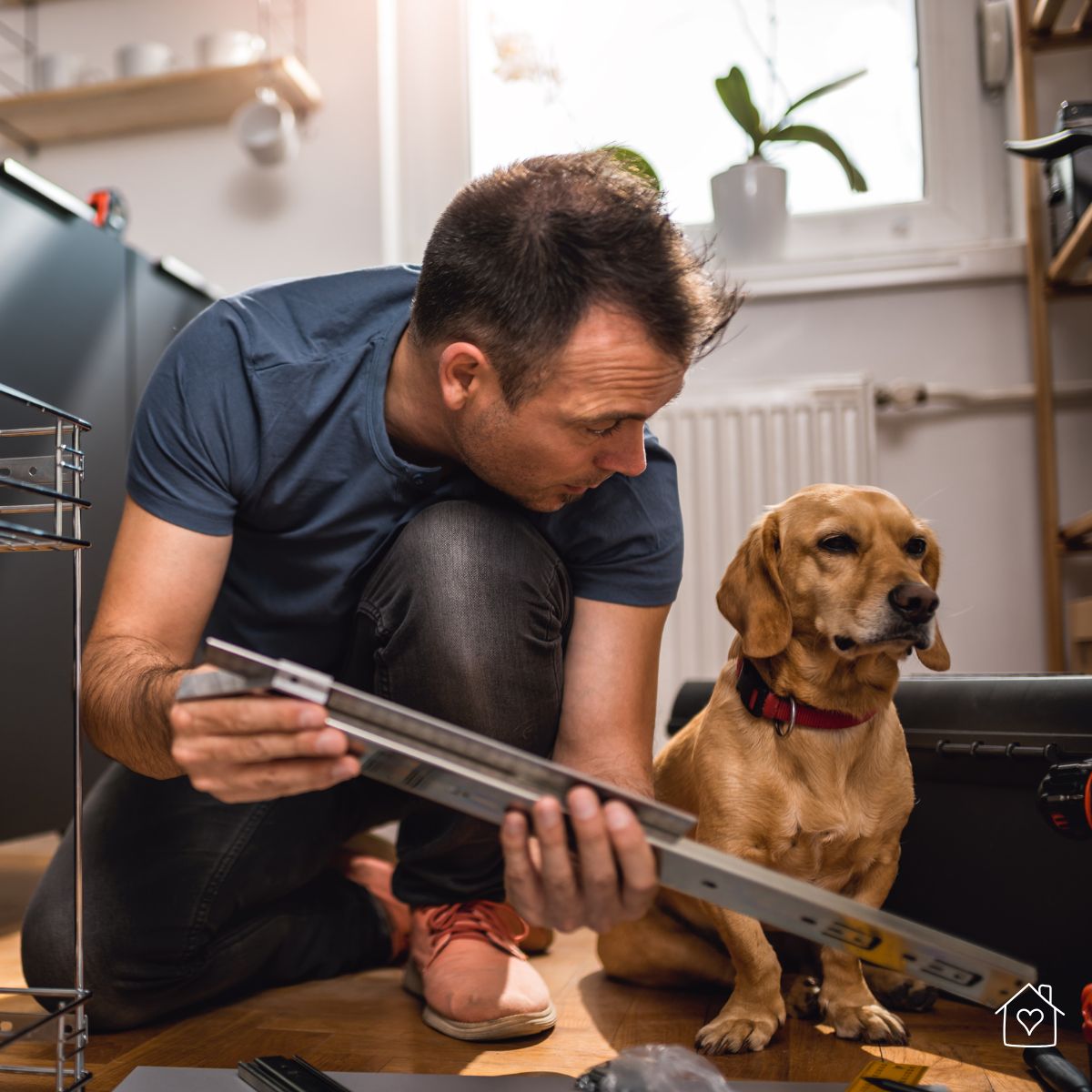 Homeowner kneels on the floor checking a metal drawer slide while a small dog looks on.