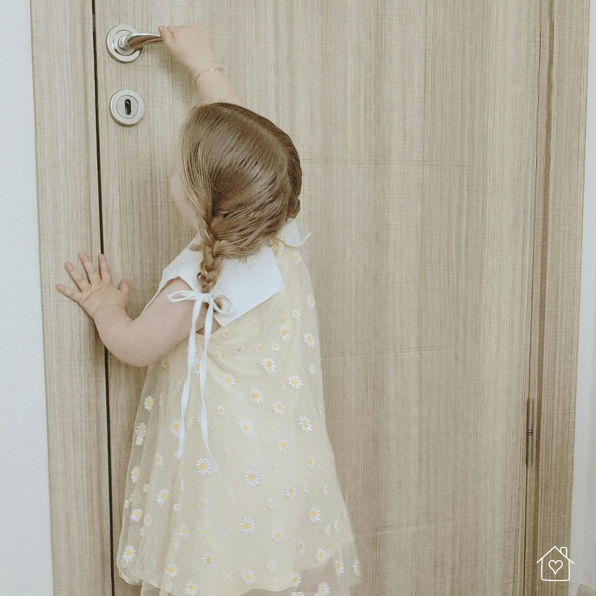 A small child in a yellow dress reaches up to open a wooden door, highlighting the importance of using childproof locks for safety at home.