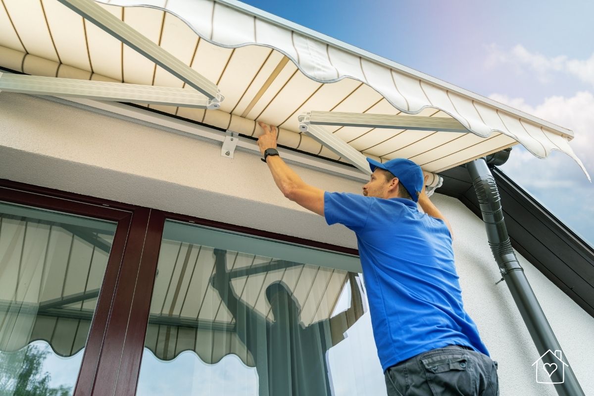 Technician mounting a white retractable awning to a stucco exterior