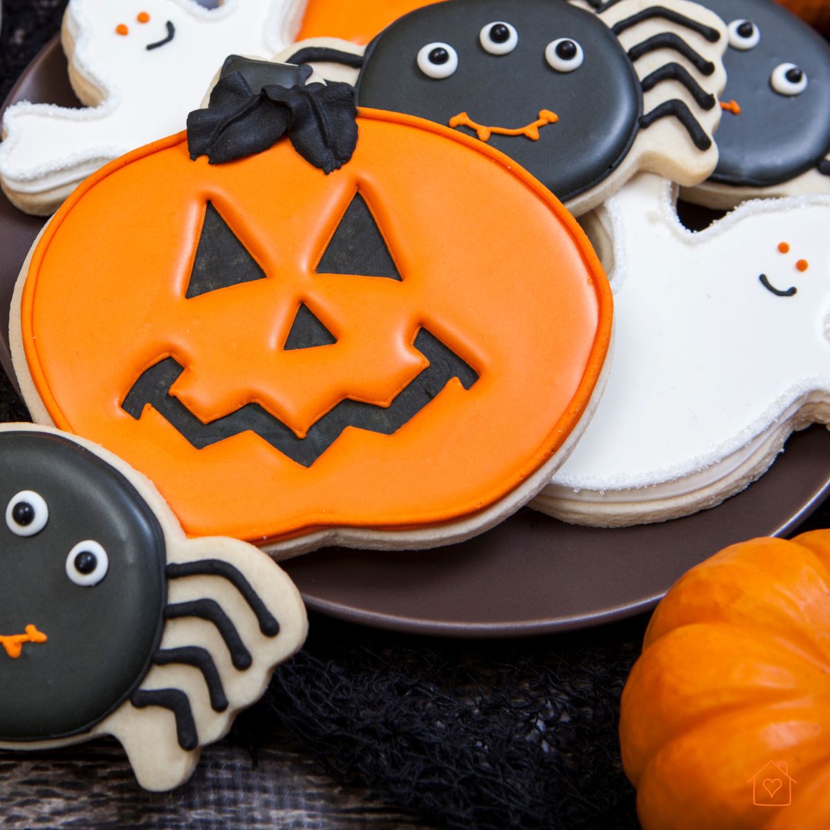 Frosted sugar cookies decorated as pumpkins, spiders, and ghosts on a dark plate.