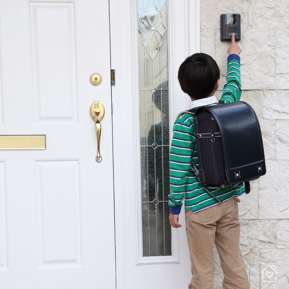 A young boy with a backpack presses a doorbell outside a home’s front door, representing safe entry practices and secure home access for children.
