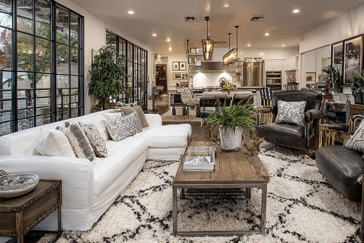 Stylish living area with a mix of leather and white sofas, wood coffee table, and black framed windows leading into an open kitchen and dining area.